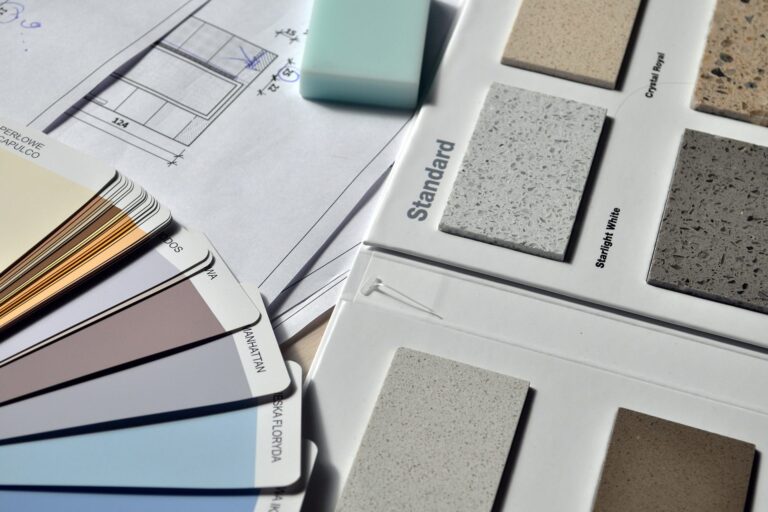 A selection of paint color swatches, countertop samples, a mint green eraser, and a technical drawing are arranged on a flat surface, suggesting interior design or renovation planning.