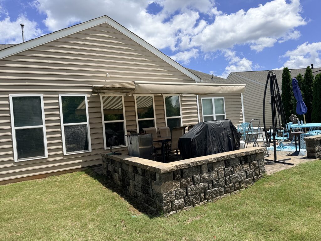 A backyard with a patio area, grill covered with a black cover, outdoor furniture, an umbrella, and a small pool. The house has beige siding and several windows—perfect for relaxing or entertaining guests. As a sunpro dealer property, it showcases ideal outdoor enjoyment even under partly cloudy skies.