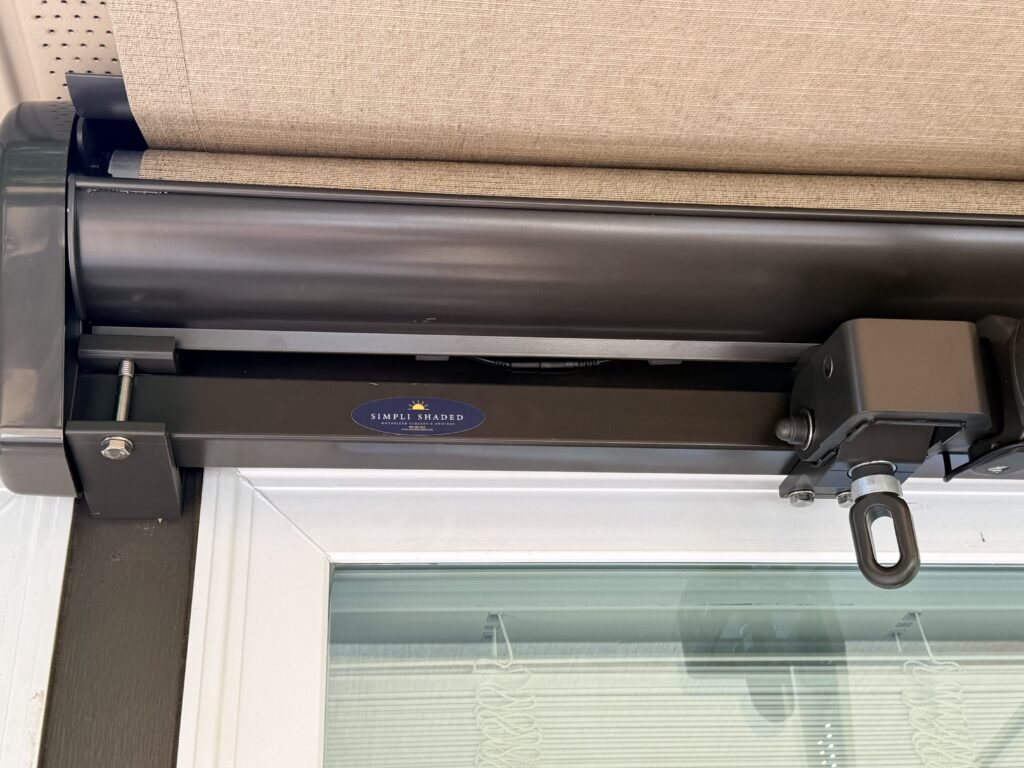 Close-up of the top part of a beige roller shade attached above a glass door, showing the Simple Shades brand label on a black mounting bracket—available from your local SunPro dealer.